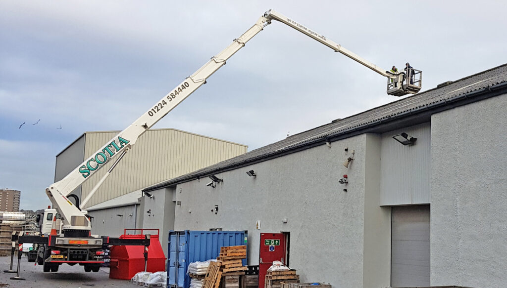 Crane lifting workmen on to high roof